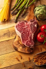 Fresh raw piece of marbled beef steak with fresh vegetables and Italian spaghetti, on a roasting board, on a wooden background. Restaurant menu, home menu. Delicious food, gastronomy