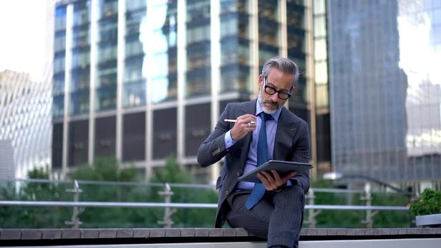 Thoughtful businessman working on financial report planning strategy for startup sitting on urban setting, pensive male expert in eyewear writing publication information by stylus pen