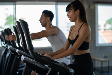 Fototapeta na wymiar Defocused blurred medium shot of active man and woman smiling while doing aerobic cardio workout on training exercise bike at the fitness gym. Healthy weight loss fit and firm concept.