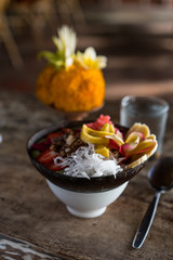 smoothie bowl in a coconut shell plate with with strawberries, chia seeds, banana, granola, flower on wooden background