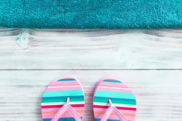 Flip-flops on white wooden background with blue towel on top side.
