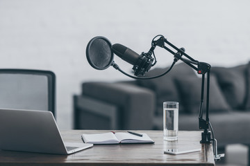 microphone, laptop, notebook and glass of water on wooden table in broadcasting studio