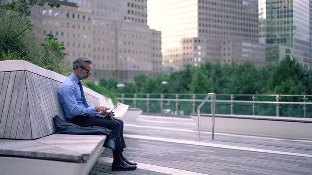 Side view of concentrated business man typing feedback for offer on touch pad sitting on urban setting, professional marketing expert doing remote job using 4g wireless internet