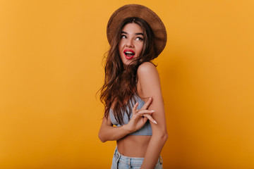 Charming girl with tanned skin looking up with smile. Enchanting european woman in brown hat...