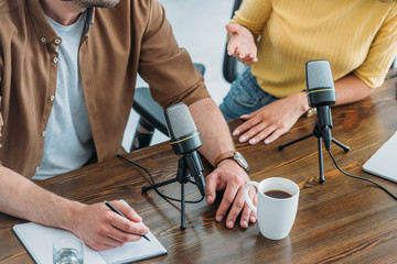 partial view of two radio hosts sitting at workplace in broadcasting studio