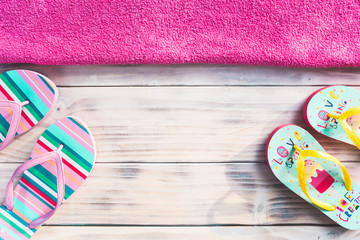 Colorful flip-flops on white wooden background with pink towel on top side.