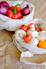 Red onion, red pepper, mushrooms and cherry tomatoes in two reusable eco friendly cotton fabric bags. Zero waste concept. Top view, close up, copy space.