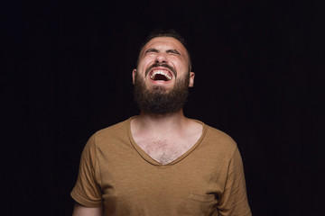 Obraz premium Close up portrait of young man isolated on black studio background. Photoshot of real emotions of male model. Crying throught laughting and smiling. Facial expression, human emotions concept.