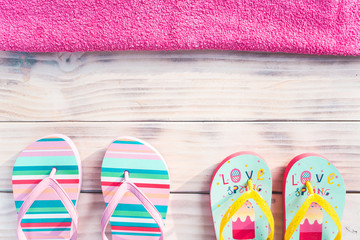 Colorful flip-flops on white wooden background with pink towel on top side.