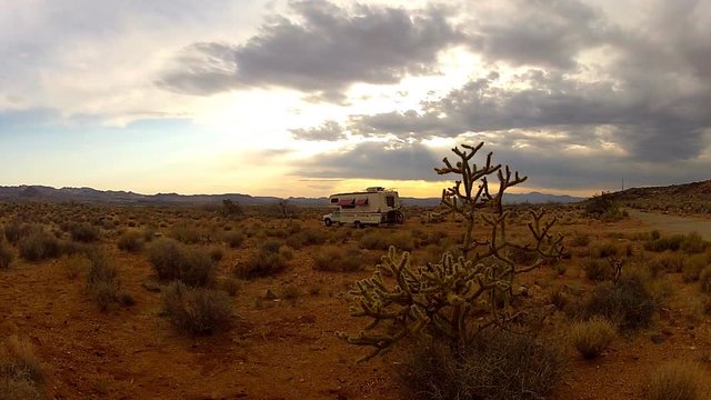 Distant RV In Desert With Cactus Bush And Setting Sun