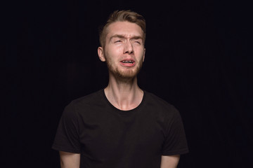 Fototapeta premium Close up portrait of young man isolated on black studio background. Photoshot of real emotions of male model. Crying, sad, dreary and hopeless. Facial expression, human emotions concept.