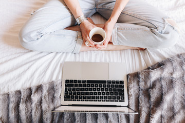 unrecognized woman drinking coffee and watching a Tv series on her laptop