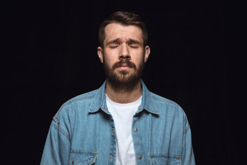 Close up portrait of young man isolated on black studio background. Photoshot of real emotions of male model. Crying with closed eyes, sad and hopeless. Facial expression, human emotions concept.