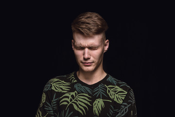 Close up portrait of young man isolated on black studio background. Photoshot of real emotions of male model. Crying with closed eyes, sad and hopeless. Facial expression, human emotions concept.