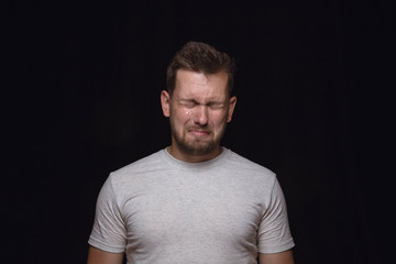 Close up portrait of young man isolated on black studio background. Photoshot of real emotions of male model. Crying with closed eyes, sad and hopeless. Facial expression, human emotions concept.