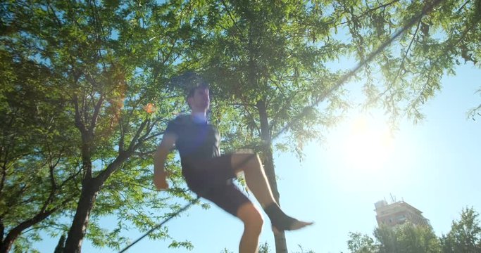 Young man performing as acrobat and training with slackline outdoors. Athlete doing sport activity and exercising with trickline in city park. Slow motion