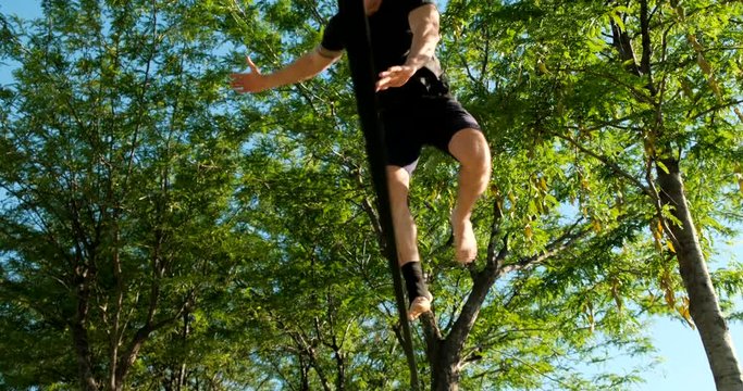 Young man performing as acrobat and training with slackline outdoors. Athlete doing sport activity and practicing with trickline in city park. Slow motion