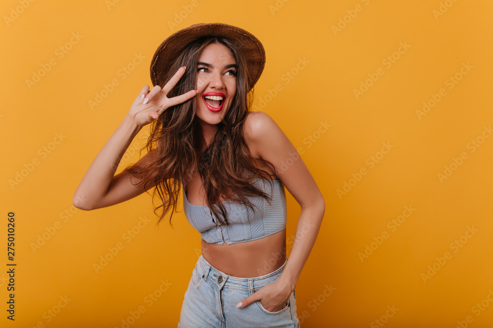 Wall mural blissful woman with trendy makeup posing with peace sign and laughing. studio portrait of graceful l