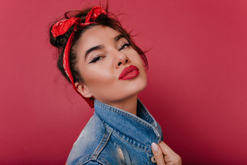 Fototapeta premium Close-up portrait of fascinating black-haired girl with red lips. Lovable female model with trendy vintage hairstyle posing with kissing face expression.