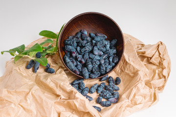 Still life with blue berries of honeysuckle, poured from a wooden cup, a branch with green leaves on a crumpled piece of paper. Close-up. Healthy food.