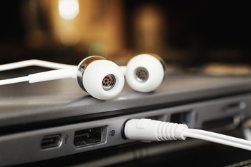 Two white earphones and mini jack plugged into laptop