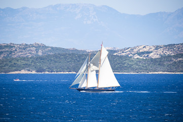 Stunning view of a beautiful sailboat sailing on the Mediterranean sea that bathes the coasts of Sardinia. Maddalena Archipelago National Park in the background, Sardinia, Italy.