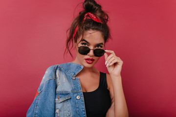 Fashionable dark-haired woman in black sunglasses looking with interest on claret background....
