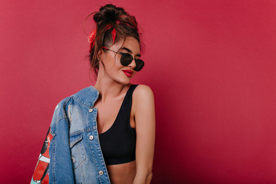 Interested Girl With Short Brown Hair Posing On Claret Background. Stylish Young Woman In Black Sunglasses And Sport Tank-top Enjoying Photoshoot.