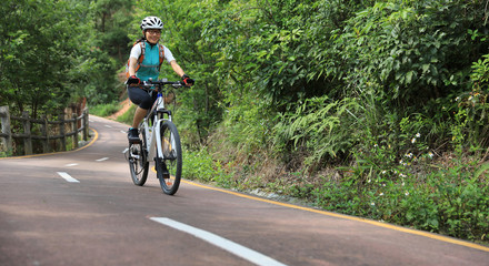 Naklejka premium Woman cyclist riding mountain bike on forest trail