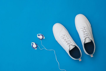 White men's sneakers and over-ear headphones on a blue background. Sports style. Flat lay.