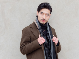 Portrait of Chinese young mustached man looking at camera with gray wall background, front view.