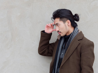 Portrait of Chinese young mustached man put his hand on his forehead with gray wall background,...
