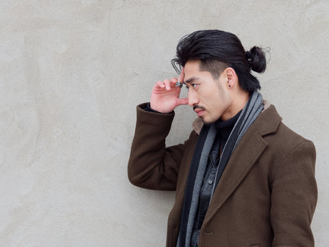 Portrait of Chinese young mustached man put his hand on his forehead with gray wall background, thinking, side view.