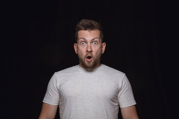 Obraz premium Close up portrait of young man isolated on black studio background. Photoshot of real emotions of male model. Wondering, exciting and astonished. Facial expression, human emotions concept.
