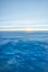Fototapeta na wymiar Blue sky with view from airplane window high angle from plane and sun setting above ocean horizon blurry background