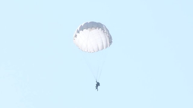 parachutist down to earth on a white parachute. A soldier on a parachute preparing to land. war games.