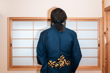 Traditional japanese house with sliding door window with back of man in kimono costume standing with obi sash belt