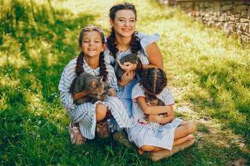 three beautiful and cute girls in blue dresses with beautiful hairstyles and make-up sitting in a sunny green garden and playing with a cats