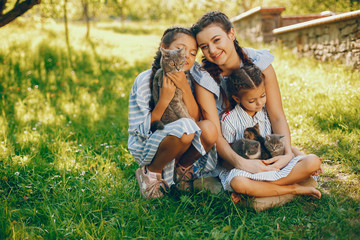 three beautiful and cute girls in blue dresses with beautiful hairstyles and make-up sitting in a sunny green garden and playing with a cats