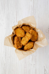 Chicken nuggets in a paper box over white wooden surface. Overhead, from above, flat lay. Close-up.