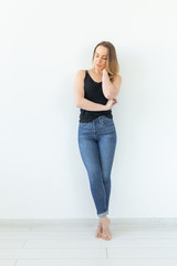 Style and people concept - young woman in jeans standing over the white wall and looks like sexy