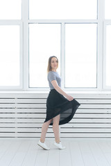 Fototapeta na wymiar Youth, style and people concept - young woman on black skirt and sneakers standing near the window
