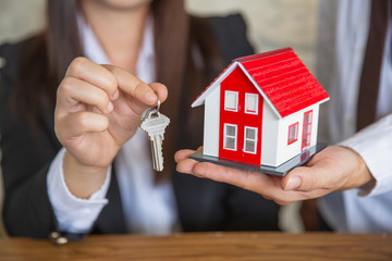 Real estate agent holding house model and keys,  customer signing contract to buy house, insurance or loan real estate.