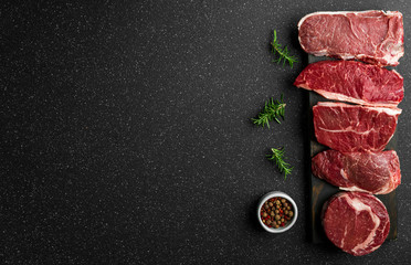Selection of raw beef meat food steaks against black stone background. New york striploin steak,...