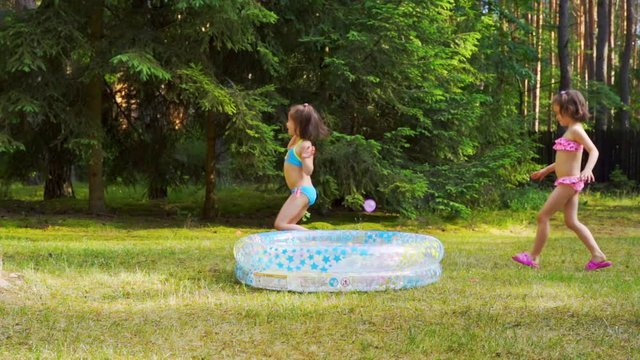 Two little girls playing with water balloons by pool on summer time