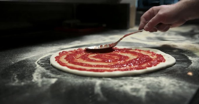 Swirling tomato red sauce on pizza dough. Authentic Neapolitan Pizza cooked in a wood fire oven.