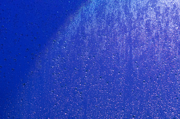 Focus and blurred photo of Rain drop on glass window with dark blue color and light reflection on it for abstract and background concept.
