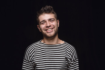 Close up portrait of young man isolated on black studio background. Photoshot of real emotions of male model. Smiling, feeling crazy happy, laughting. Facial expression, human emotions concept.