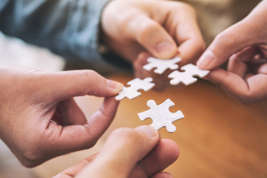 Closeup image of people's hands holding and putting a piece of white jigsaw puzzle together
