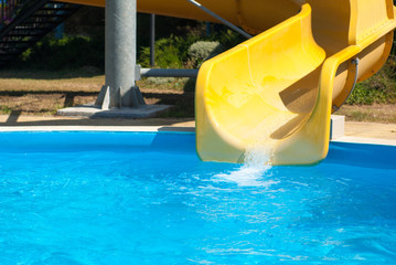 yellow water slide with blue swimming pool in aqua amusement park during summer warm sunny day